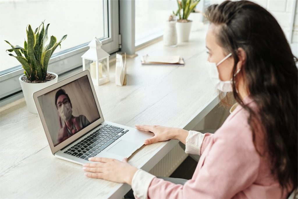 Woman wearing a mask in the office, doing a video conference call with her laptop due to the COVID-19 pandemic