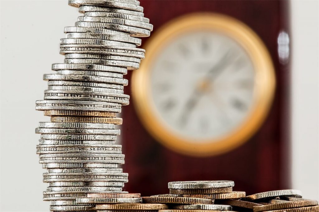 A stack of coins with a gold clock in the background, signifying cash rebates when refinancing a home loan in Singapore