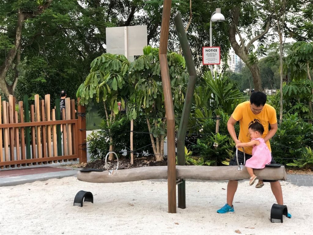 Father playing with his daughter at the HDB playground swing in Singapore.