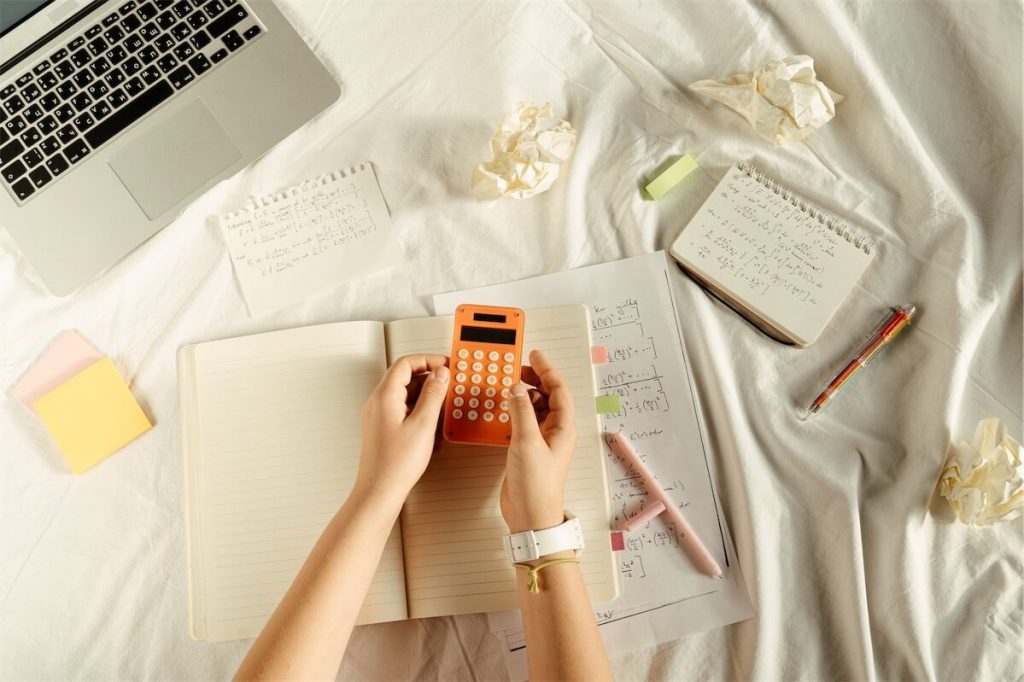 Person calculating their Home Protection Scheme (HPS) premiums with a calculator, notebook, pen and laptop.