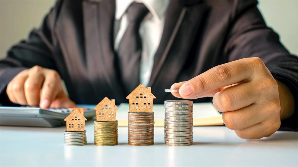 Man stacking coins and cardboard houses - depicting the varying IRAS property tax in Singapore