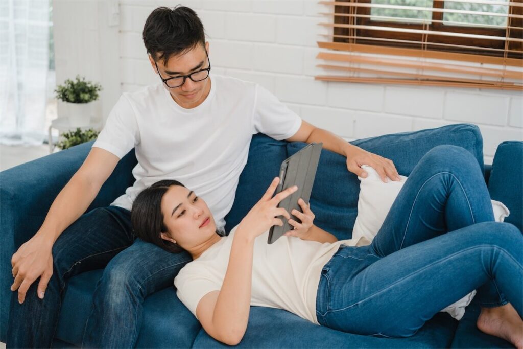 Husband and wife browsing properties on their tablet, looking to purchase a second property in Singapore