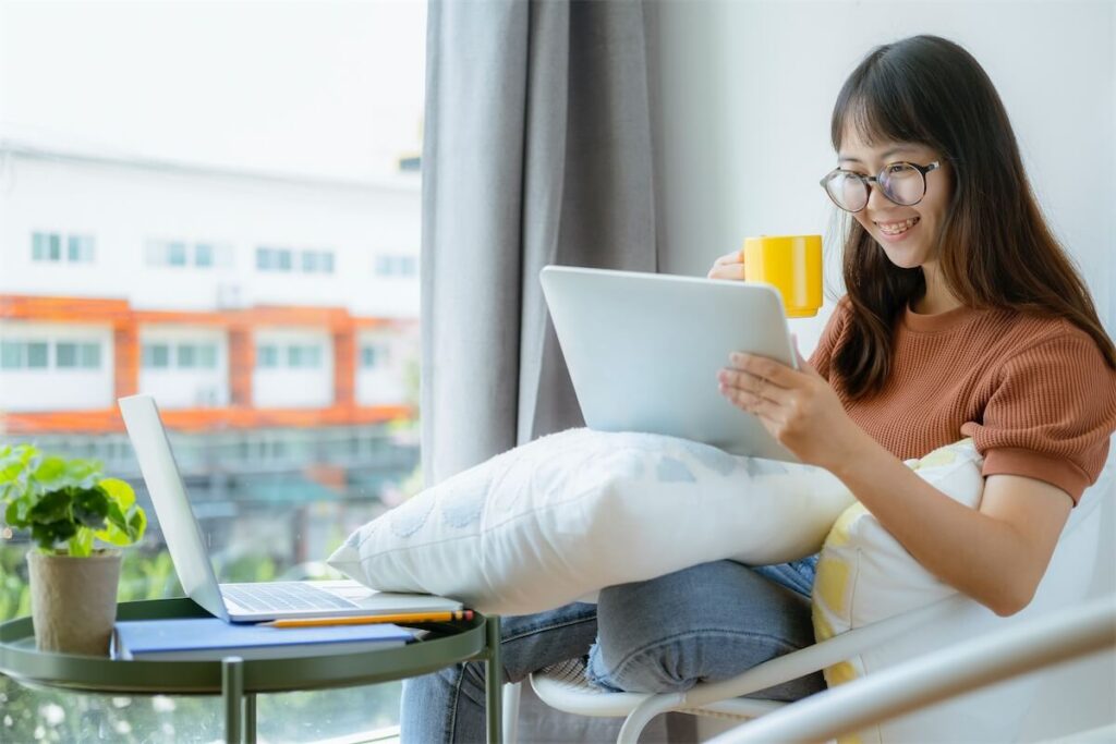 A lady using her tablet and having coffee in a co-living space - an ideal alternative housing option when HDB BTO is delayed.