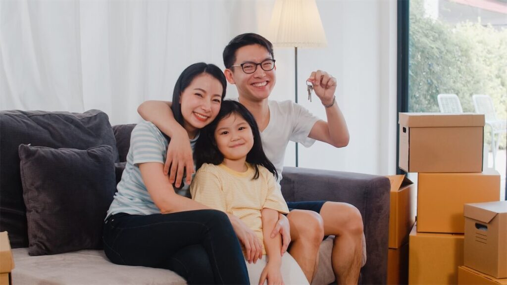  A young family holding their HDB BTO keys and moving boxes in the background, preparing to move into their new HDB BTO flat in Singapore
